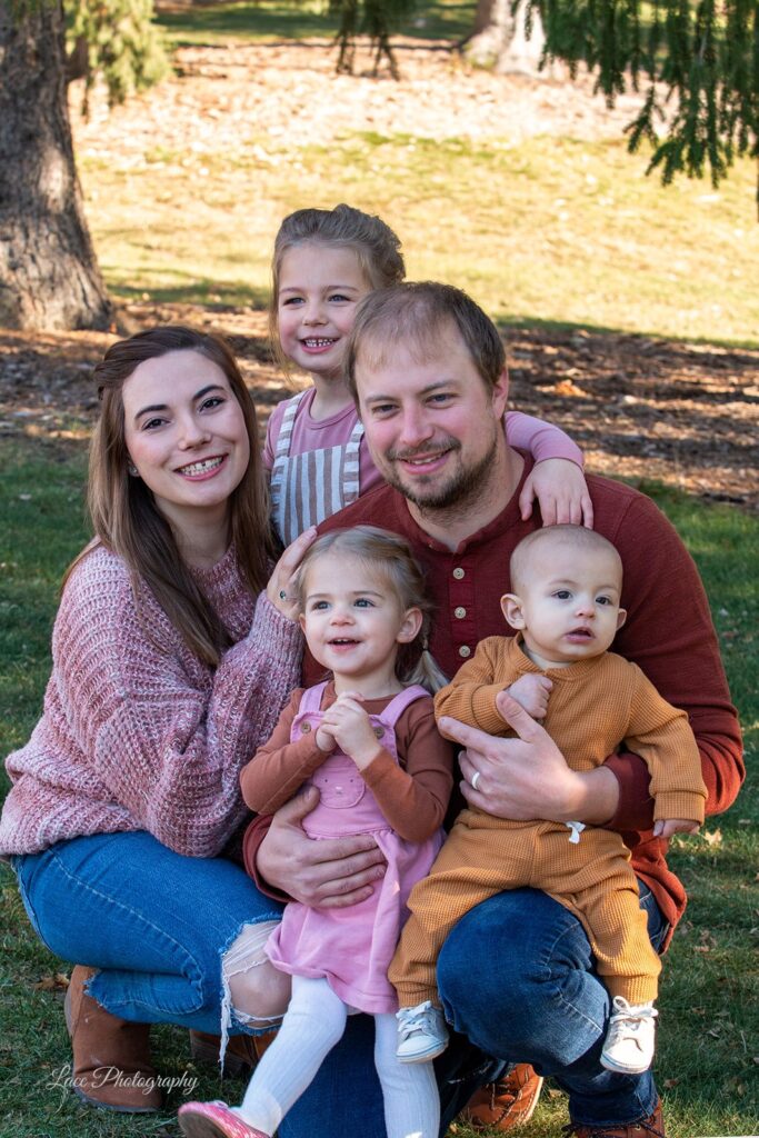 Hannah and her beautiful family: husband, two daughters and baby son kneeling on the grass posing together. Hannah is a branding expert in Waukesha and Lake Country, WI