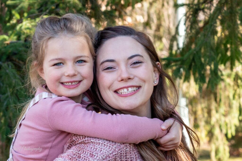 Hannah with her daughter on her back and arms around her smiling, closeup, looking at the camera