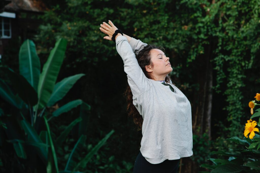 A girl doing yoga practicing wellness coaching outdoors with vibrant greenery behind her